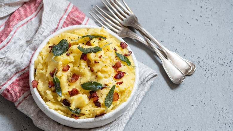 A bowl of mashed potatoes with bits of bacon and herbs