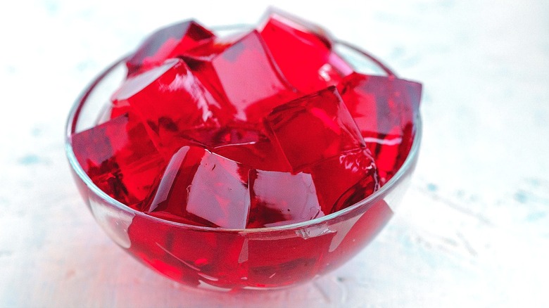 A clear bowl filled with cubes of red gelatin over a white background