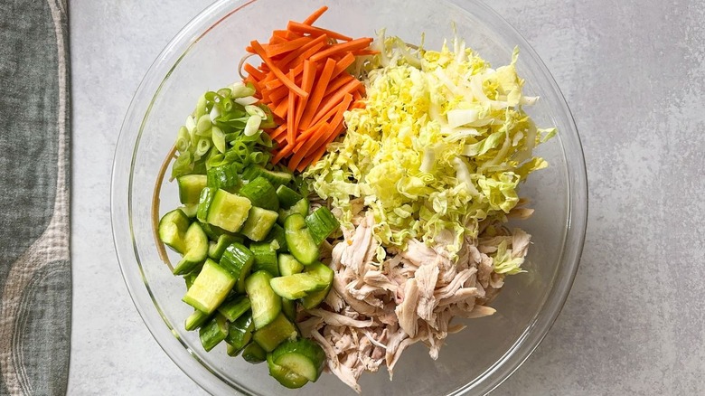 cucumbers, scallions, carrots, cabbage, and rotisserie chicken over soba noodles in large glass bowl