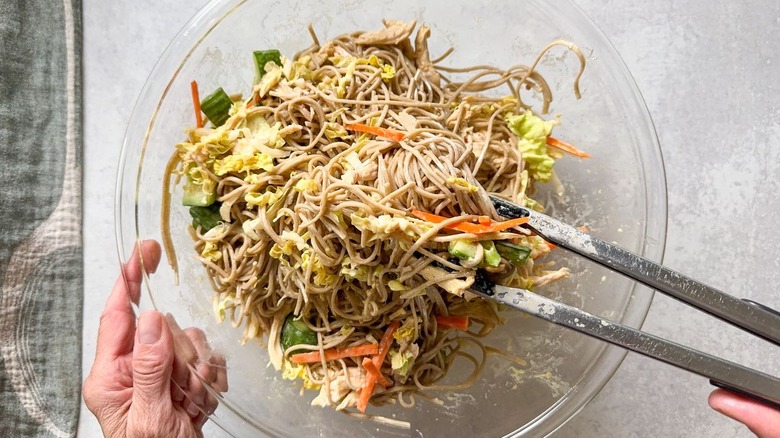 Tossing chilled soba salad with tongs in glass bowl