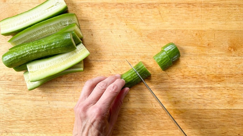 Cutting cucumber halves into  pieces on cutting board