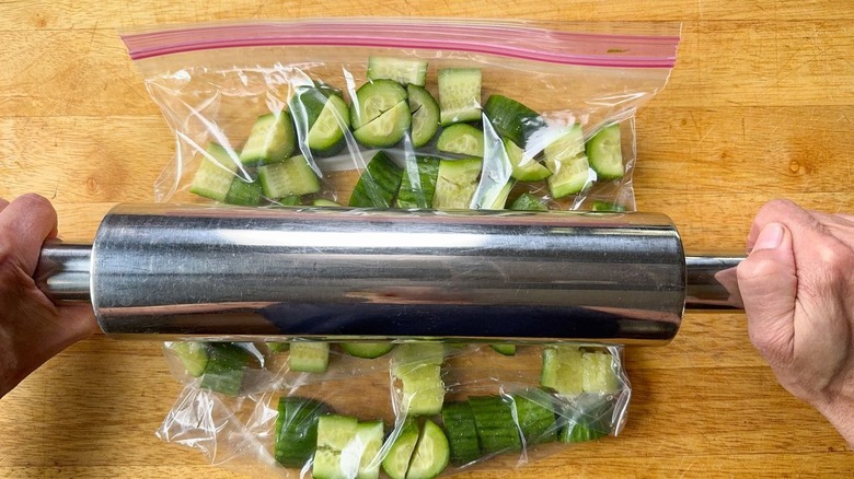 Using a rolling pin to smash cucumber slices in a ziplock bag on cutting board