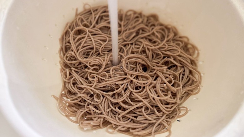Rinsing cooked soba noodles with water in colander in sink