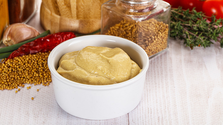 Dijon mustard served in a small condiment bowl, with greens and spices in the background