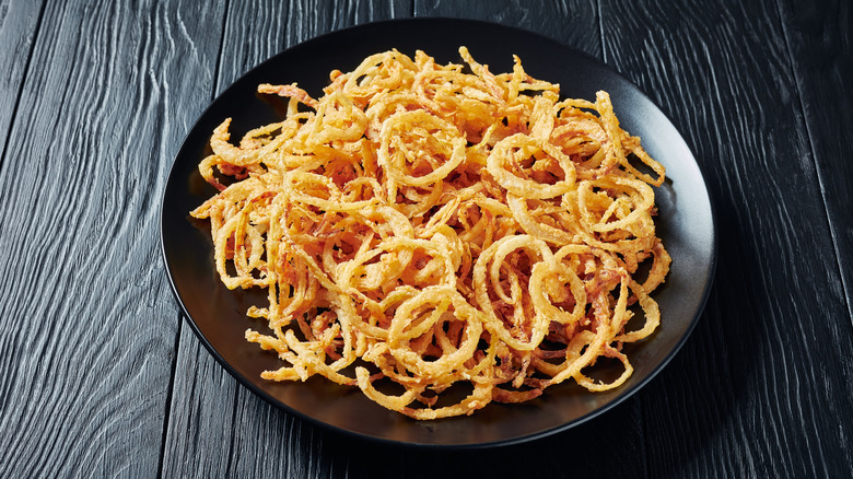 Black bowl of French fried onions on a black picnic table.