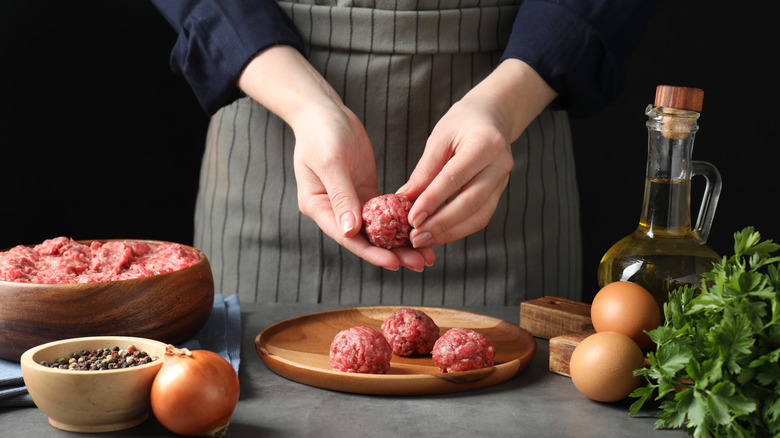 Someone forms raw meatballs.