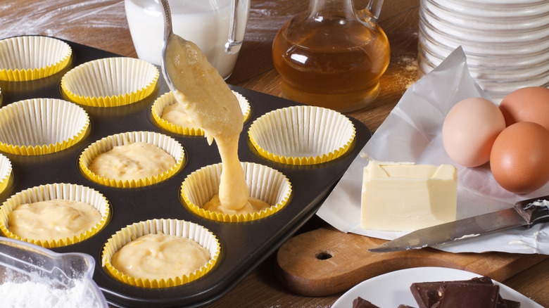 Batter fills lined muffin tin cups from a spoon.