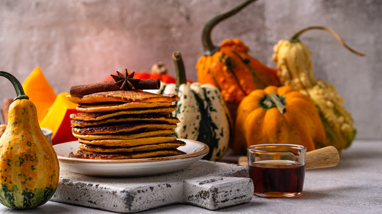 A stack of pumpkin pancakes arranged with gourds in a fall tableau.