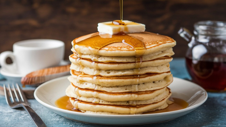 A huge stack of pancakes with butter and syrup on a plate.