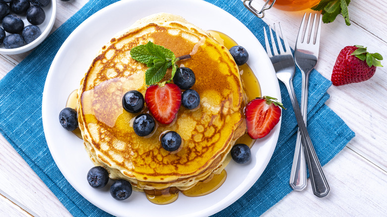 Pancakes on a white plate with syrup, berries, and a sprig of mint