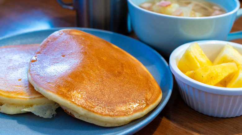 Pancakes on a blue plate with a side of pineapple