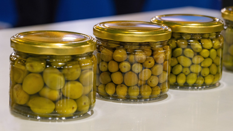 Four jar of green olives submerged in brine.