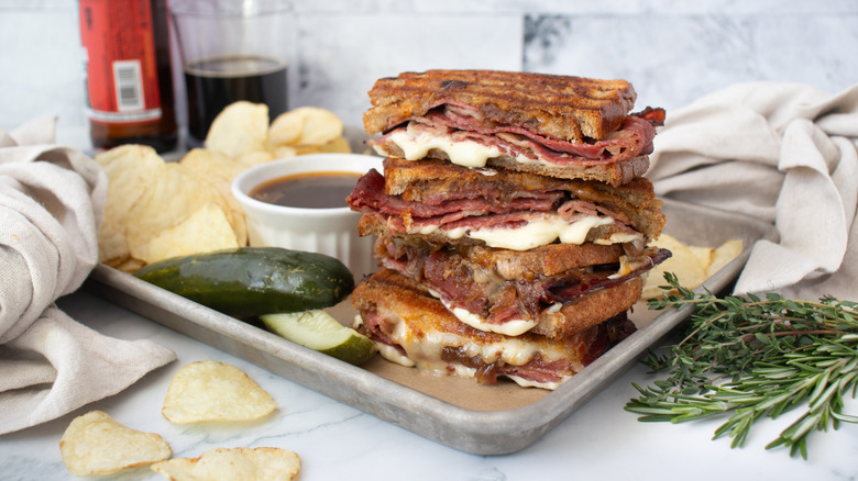 French dip pastrami sandwich stacked on serving tray
