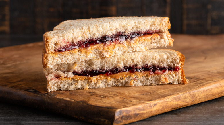 A peanut butter and jelly sandwich cut in half and stacked on a cutting board