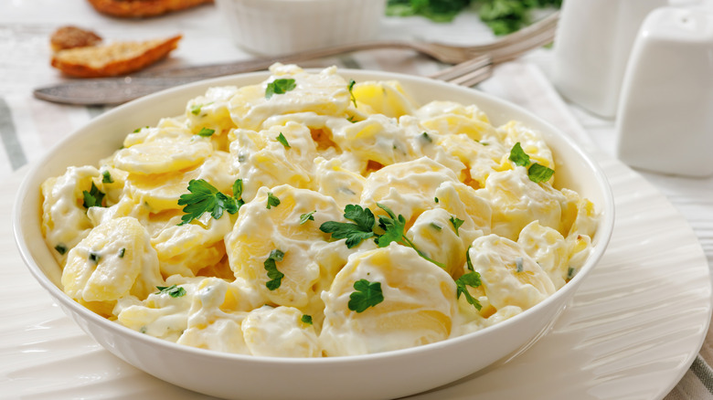 potato salad served on white wooden table with bread, sour cream, and forks