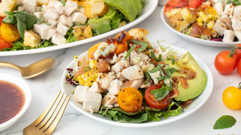 rotisserie chicken salad loaded with veggies, bacon, and raspberry dressing on a platter and two plates