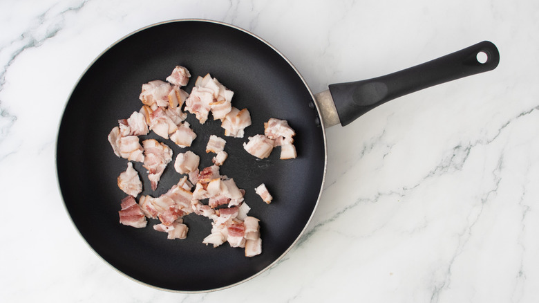 chopped bacon in skillet on marble surface