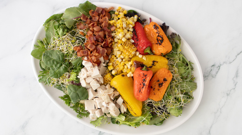 chicken and bacon salad with vegetables on a platter on top of a marble surface