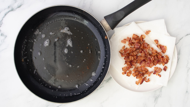 skillet with bacon grease next to crispy bacon draining on paper towel