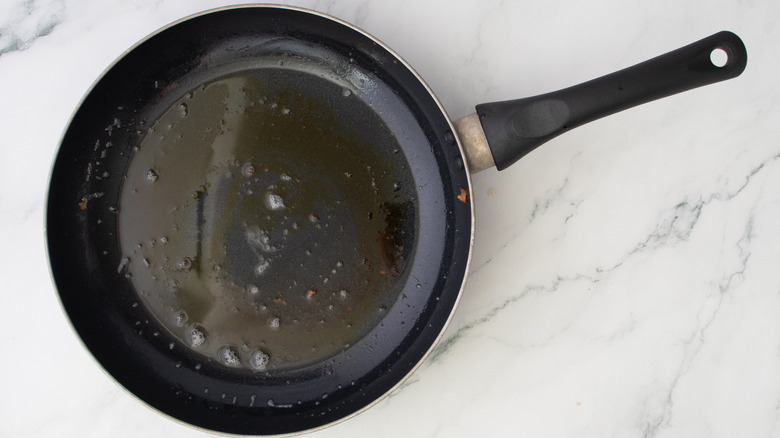 bacon drippings and oil heating in skillet on marble surface