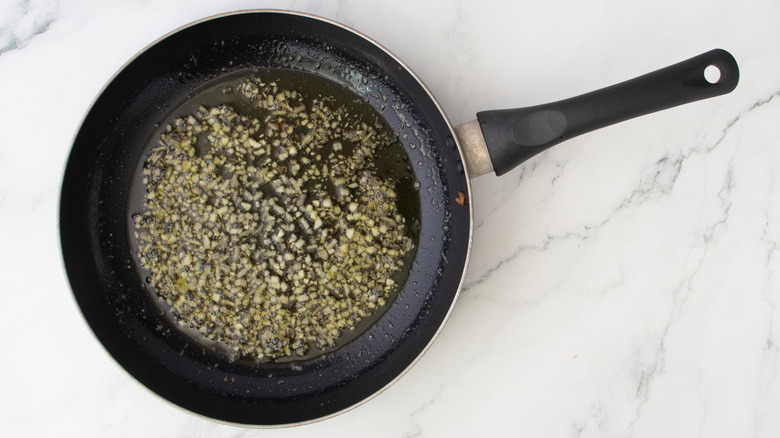 minced garlic and shallots cooking in skillet on marble surface