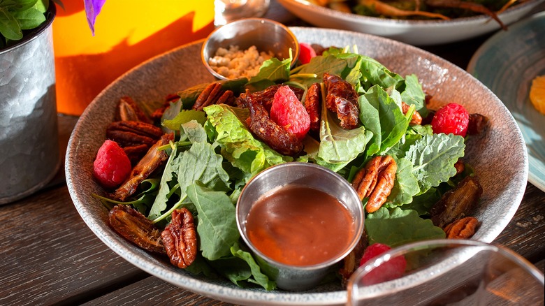 Green salad with pecans, raspberries, and raspberry dressing in a shallow gray bowl