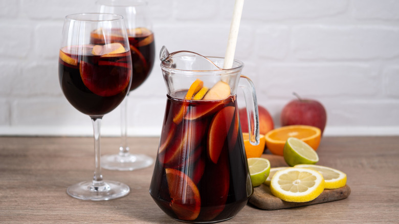 a pitcher of sangria with fruits and two filled glasses on the side