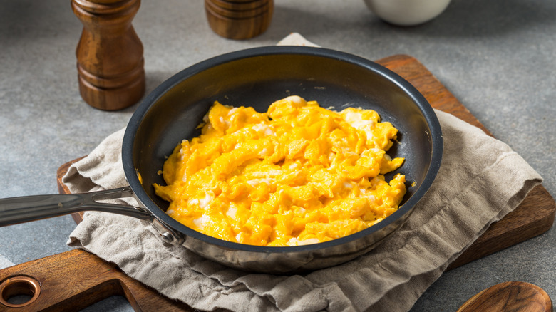 Scrambled eggs in a pan over a cloth on a wooden board