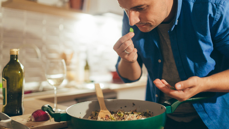 Man sniffs a mint leaf over a pan of cooking rice