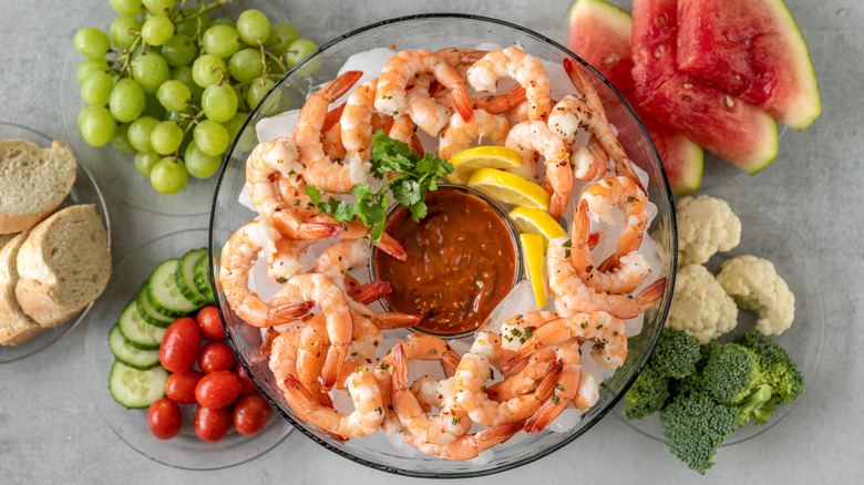 A bowl of shrimp cocktail with fruits and vegetables on the side