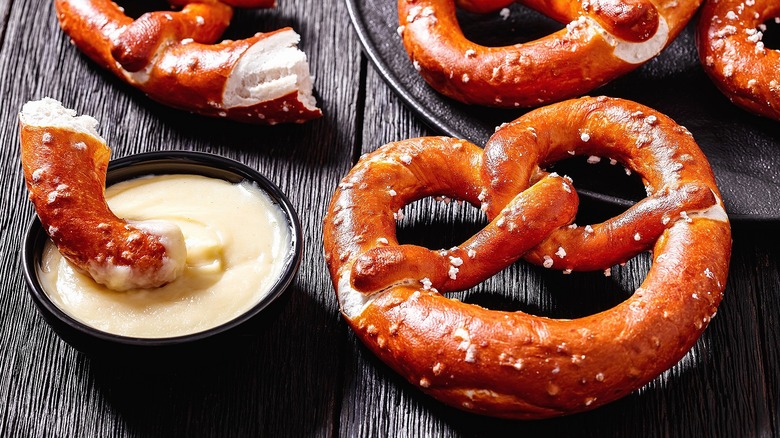 Soft pretzels covered in salt and a torn piece dipped in cheese sauce.