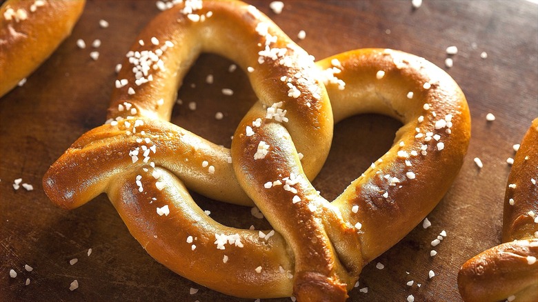 Soft pretzel covered in coarse salt on a wooden surface.