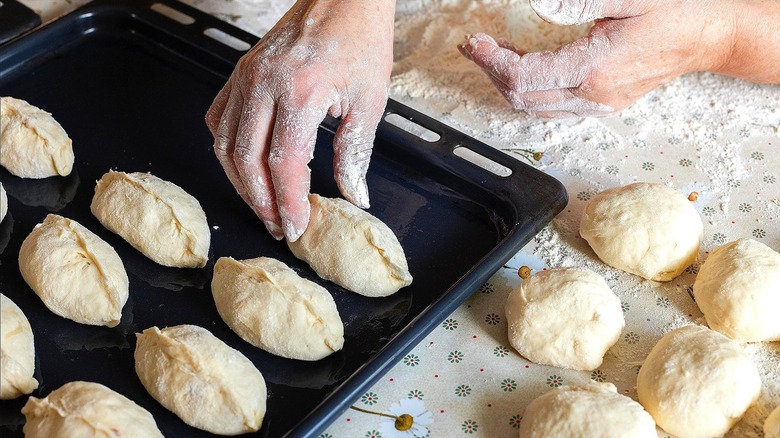 Hands forming stuffed dumplings and placing them on a coated baking tray