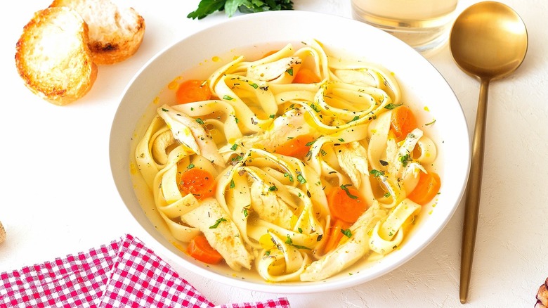 Chicken noodle soup in a white bowl with a copper spoon