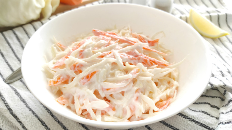 A white bowl of creamy coleslaw sits on a cloth napkin.