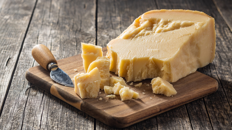 A big wedge of Parmesan with come large chunks arranged in a cutting board in a simple, rustic scene.