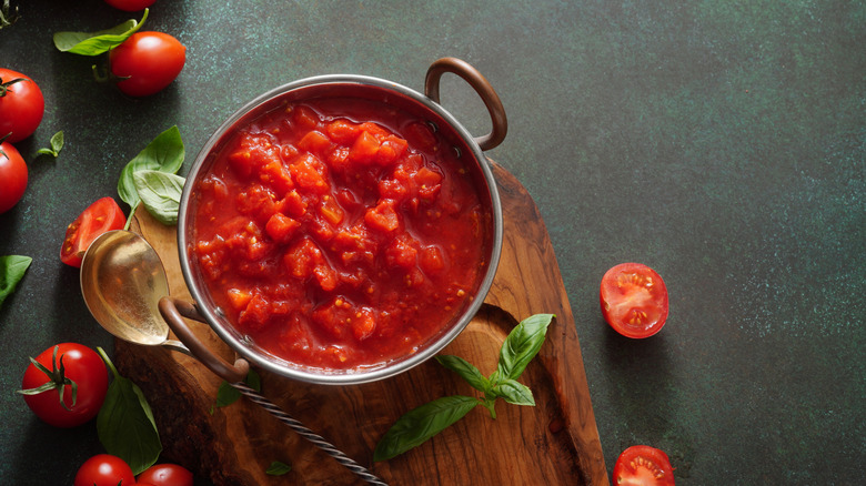 Tomato sauce in a pot on a wooden board, basil leaves and cherry tomatoes on the side