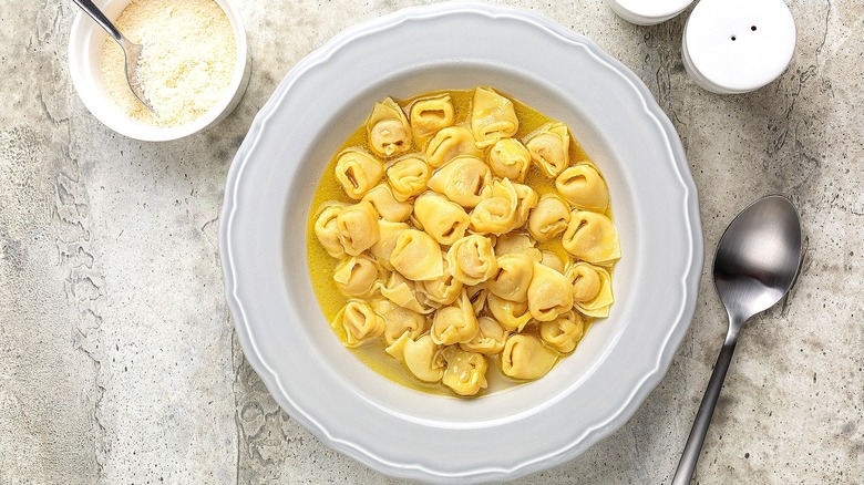 Cooked tortellini in broth in a white shallow bowl