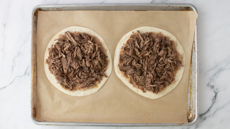 two tortillas topped with mashed beans and shredded beef