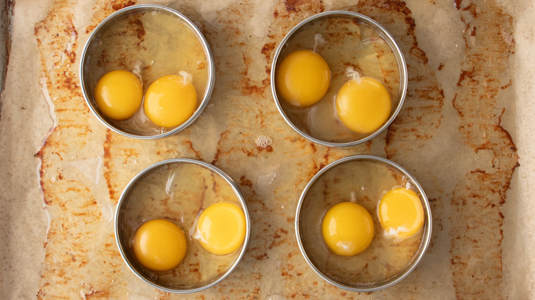 Raw eggs inside ring molds on baking sheet