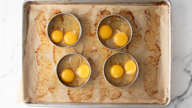 raw eggs inside ring molds in a baking pan