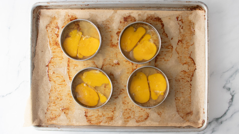 raw eggs inside ring molds in a baking pan