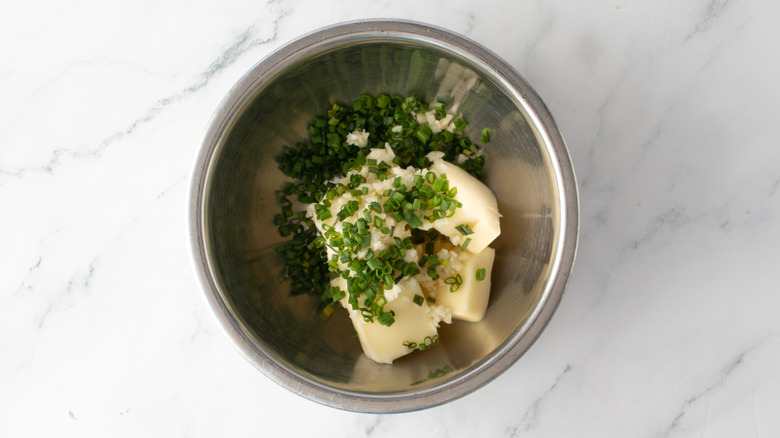butter in a bowl with chopped garlic and chives