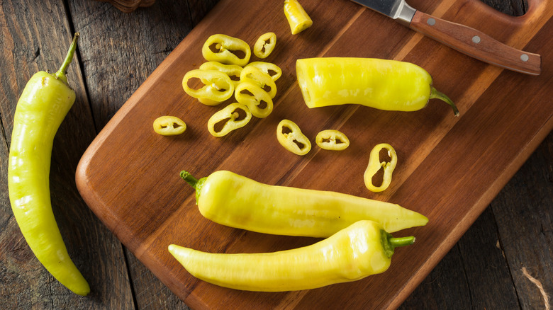Chopped and whole banana peppers on wooden board