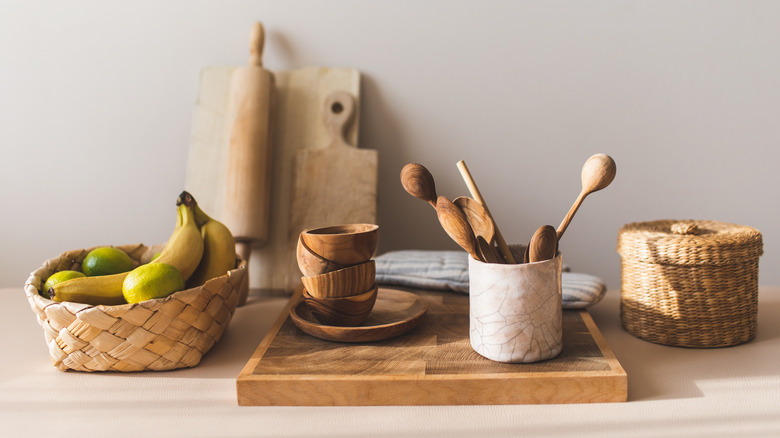 Limes and bananas in woven basket next to wooden kitchen utensils on countertop.