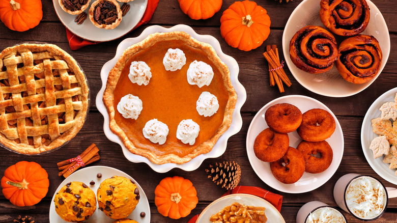 Assortment of autumn desserts on a wooden table next to multiple small pumpkins