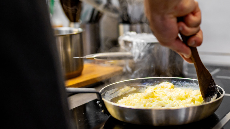 A chef cooking scrambled eggs in a pan.