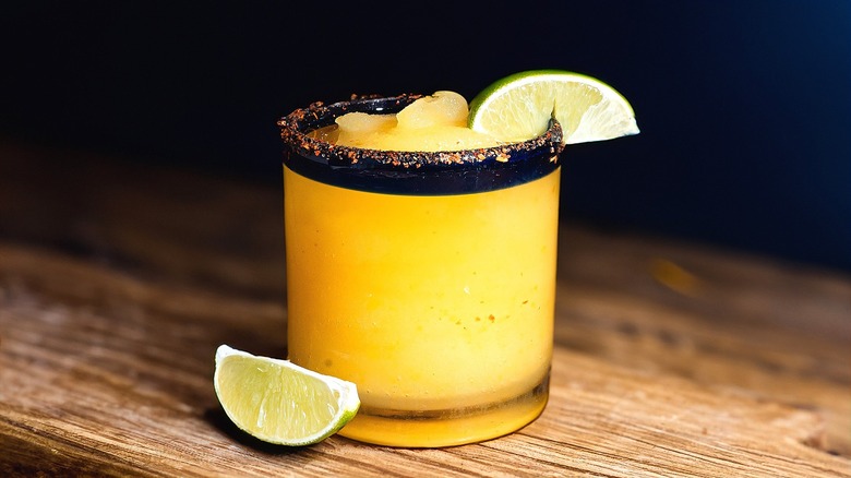 Frozen orange margarita with lime wedges in a short glass with a dark blue rim