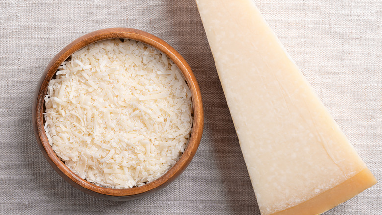 A wedge of Parmesan next to a bowl of grated parmesan