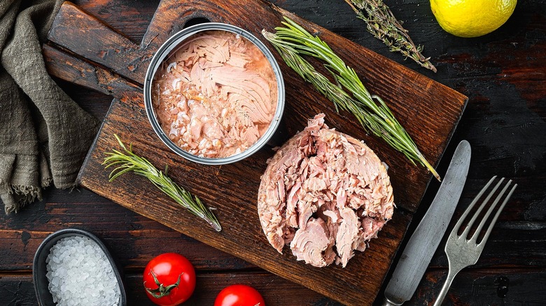 Canned tuna on a wooden cutting board with sprigs of rosemary